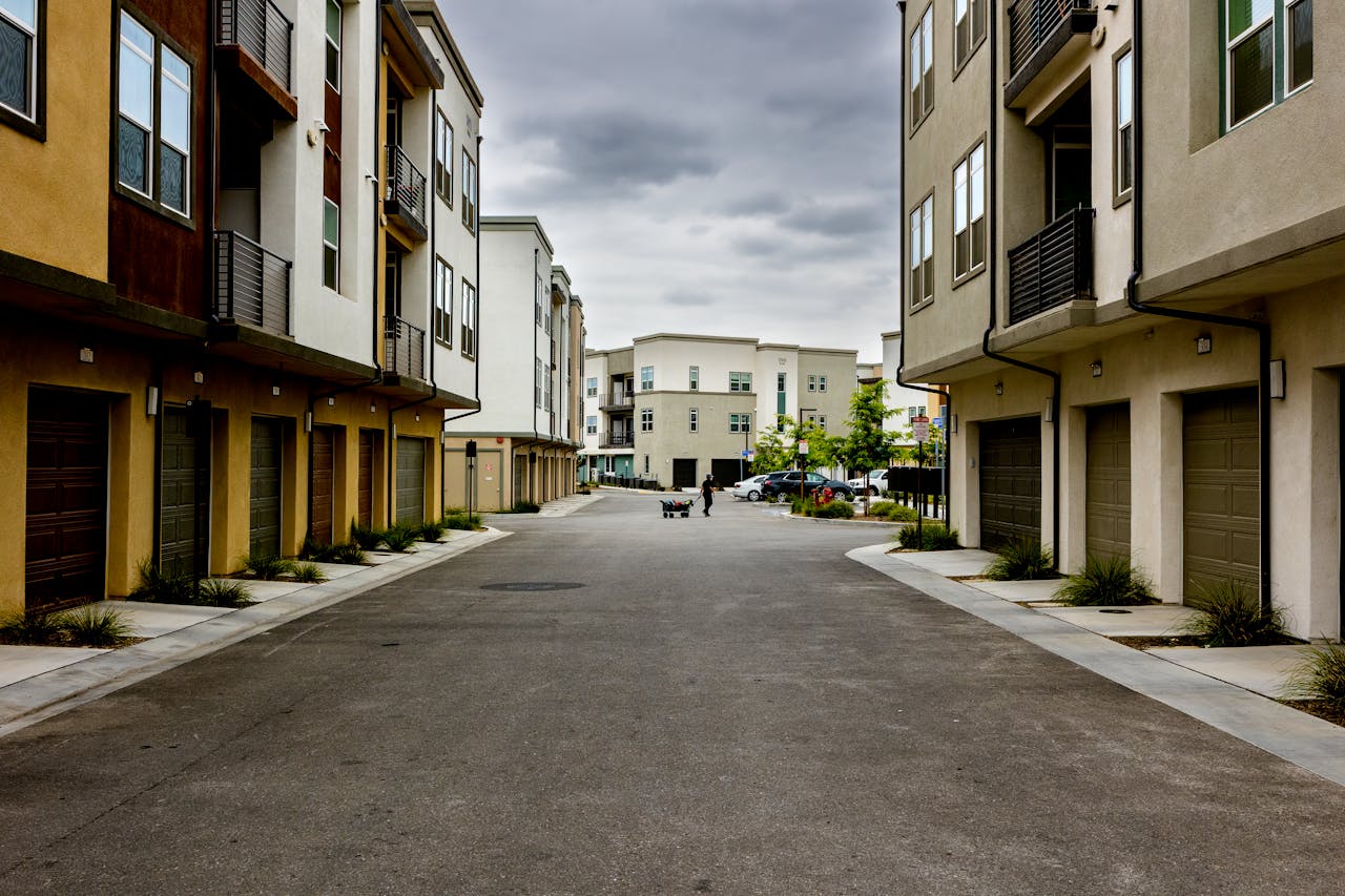 A man pulls a cart down a quiet residential street lined with modern townhouses.